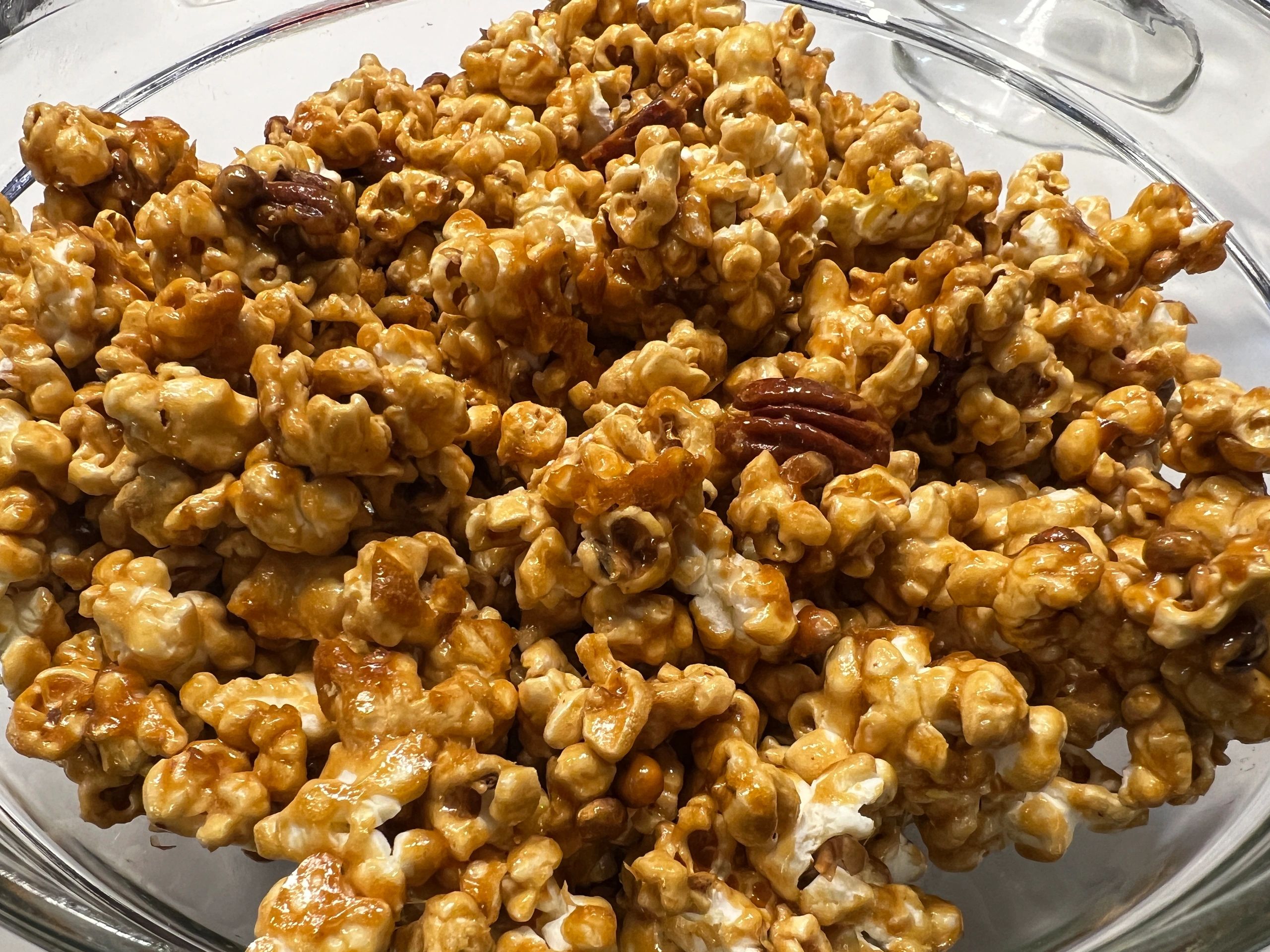 Caramel popcorn with pecans in a glass bowl.
