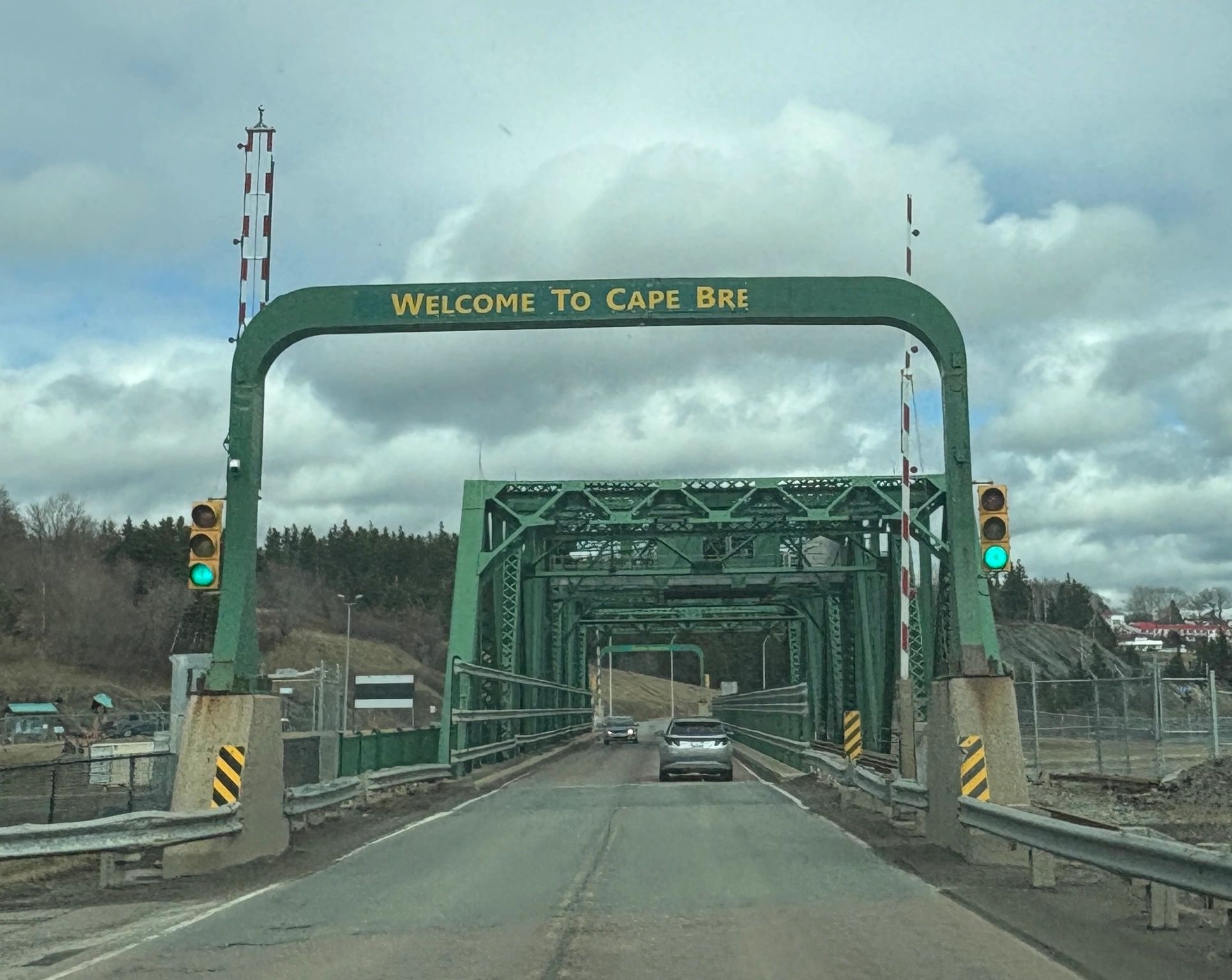 Green metal bridge entrance with a sign welcoming to Cape Breton.