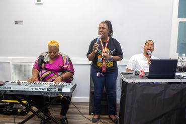 Three musicians performing together indoors with keyboard, microphone, and laptop.