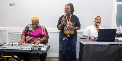 Three musicians performing indoors with keyboard and microphones.