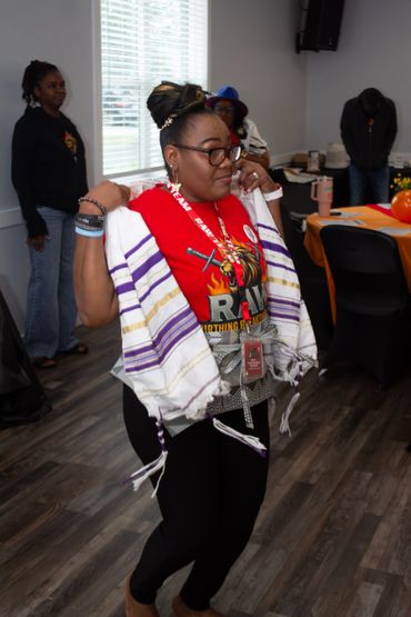 Woman wearing a red shirt and a tallit at an indoor gathering.