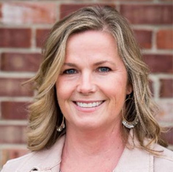 Smiling woman with blonde hair in front of a brick wall.