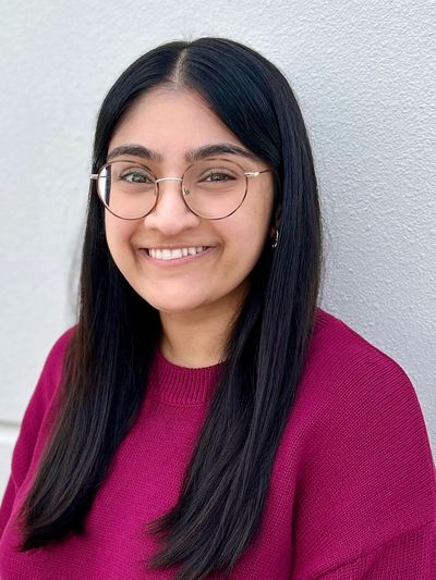 Young woman in glasses smiles warmly against a light wall background.
