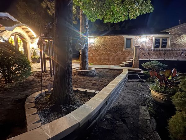 Nighttime garden with illuminated walkway and brick wall.