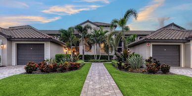 A modern house with a tiled roof, green lawn, and palm trees under a blue sky.