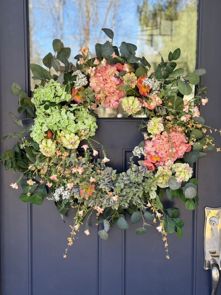 Colorful floral wreath with green and peach flowers on a dark door.