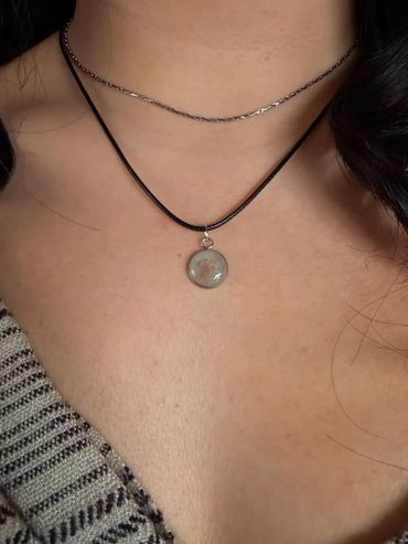 Close-up of a person wearing two necklaces, one with a round pendant.