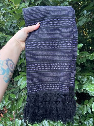 Hand holding a folded black and purple striped textile with tassels.