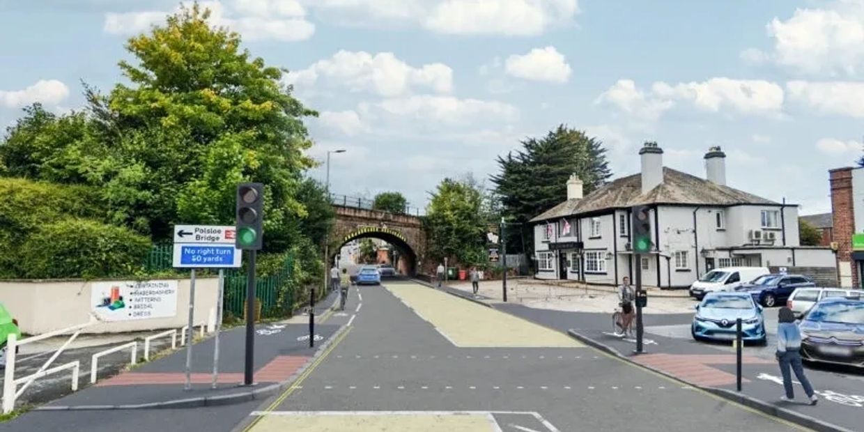 Street view with traffic lights, pedestrians, and a bridge in the background.