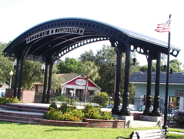 Black metal pavilion structure with American flag in a park setting.