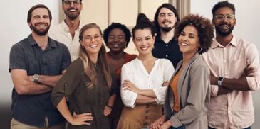 A diverse group of eight smiling young professionals posing together indoors.