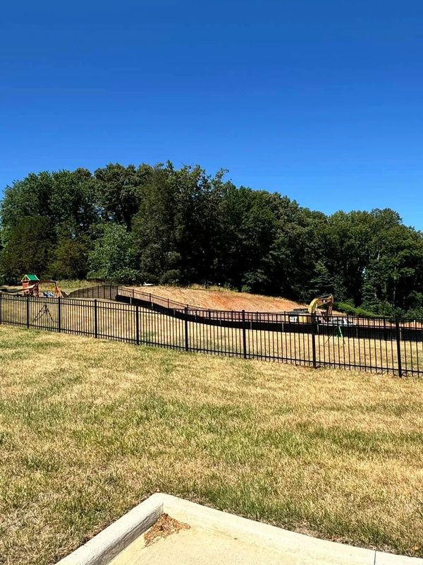 A fenced backyard with playground equipment and trees under a clear blue sky.