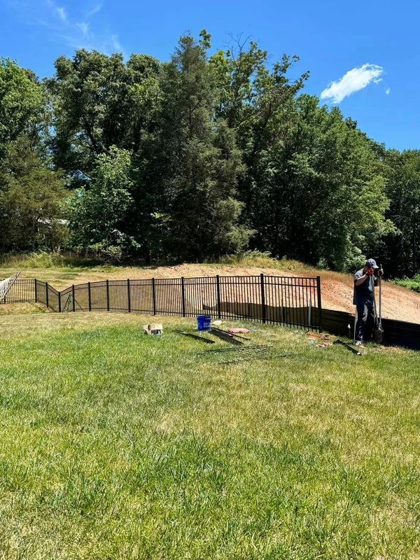 Man working on a fenced backyard with a hammock and green trees.