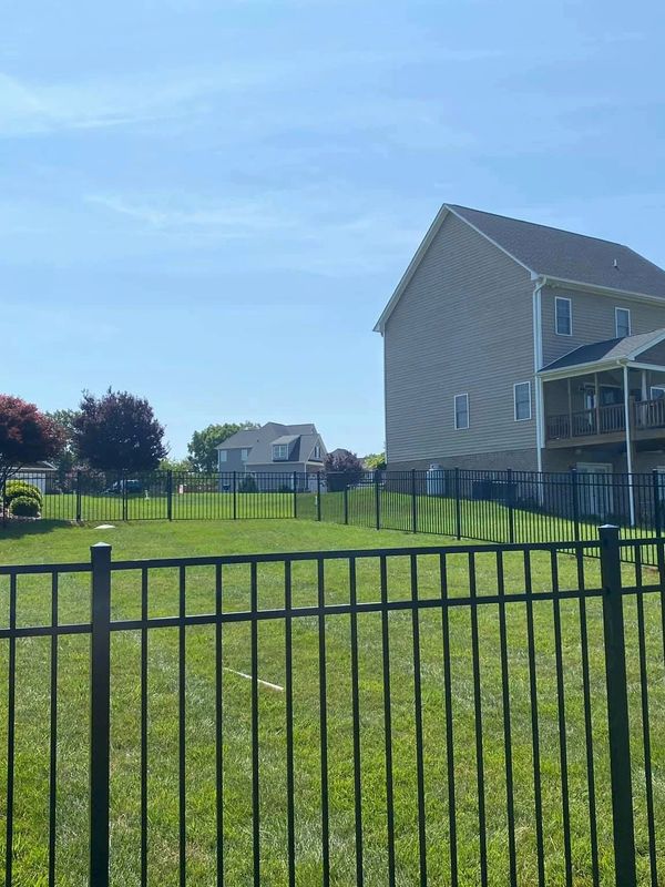 Two suburban houses with fenced green lawns under a clear blue sky.