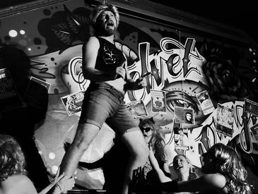 A man in shorts performs energetically on stage with a graffiti backdrop.