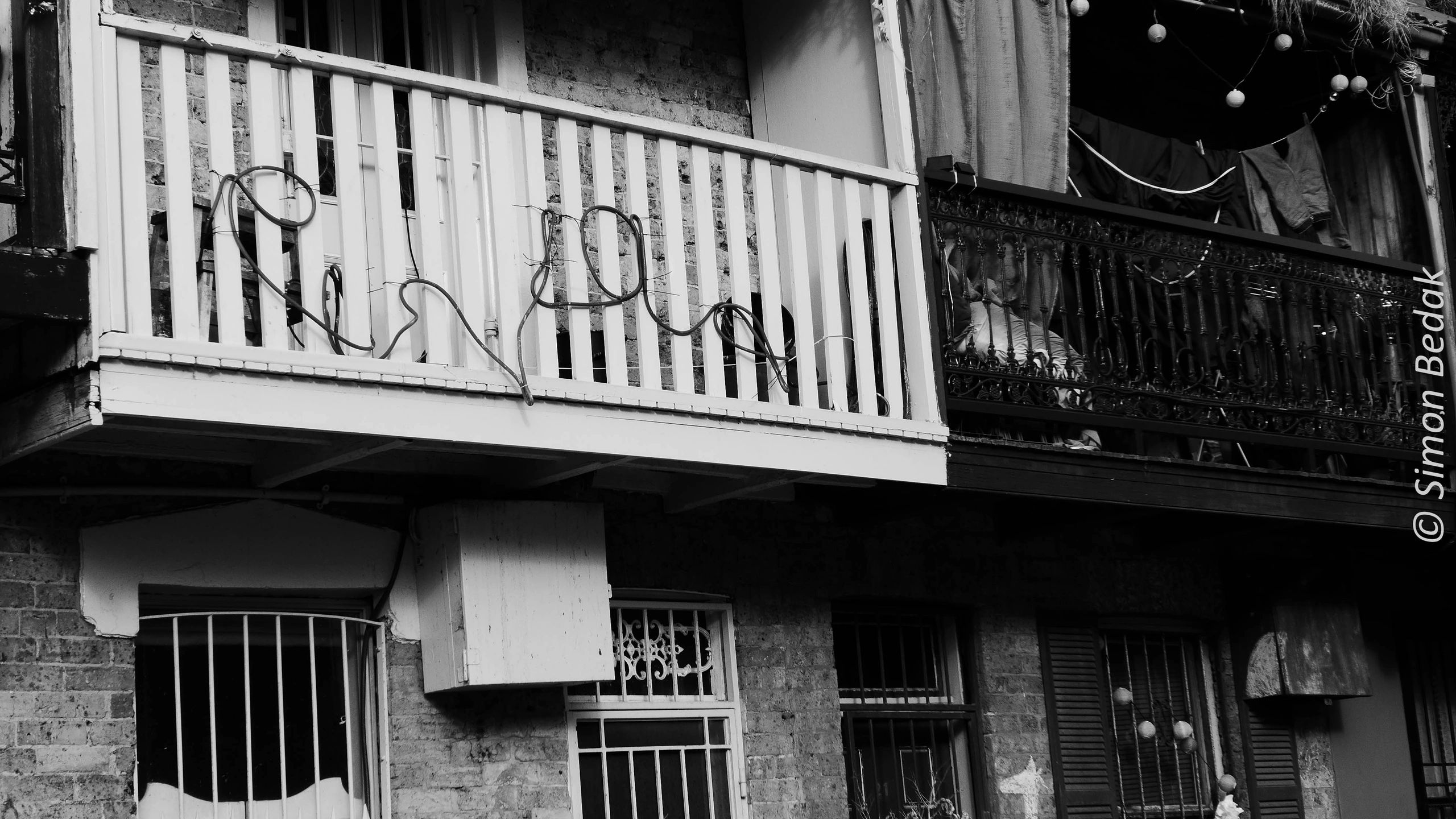 Black and white photo of two balconies with clothes and string lights.
