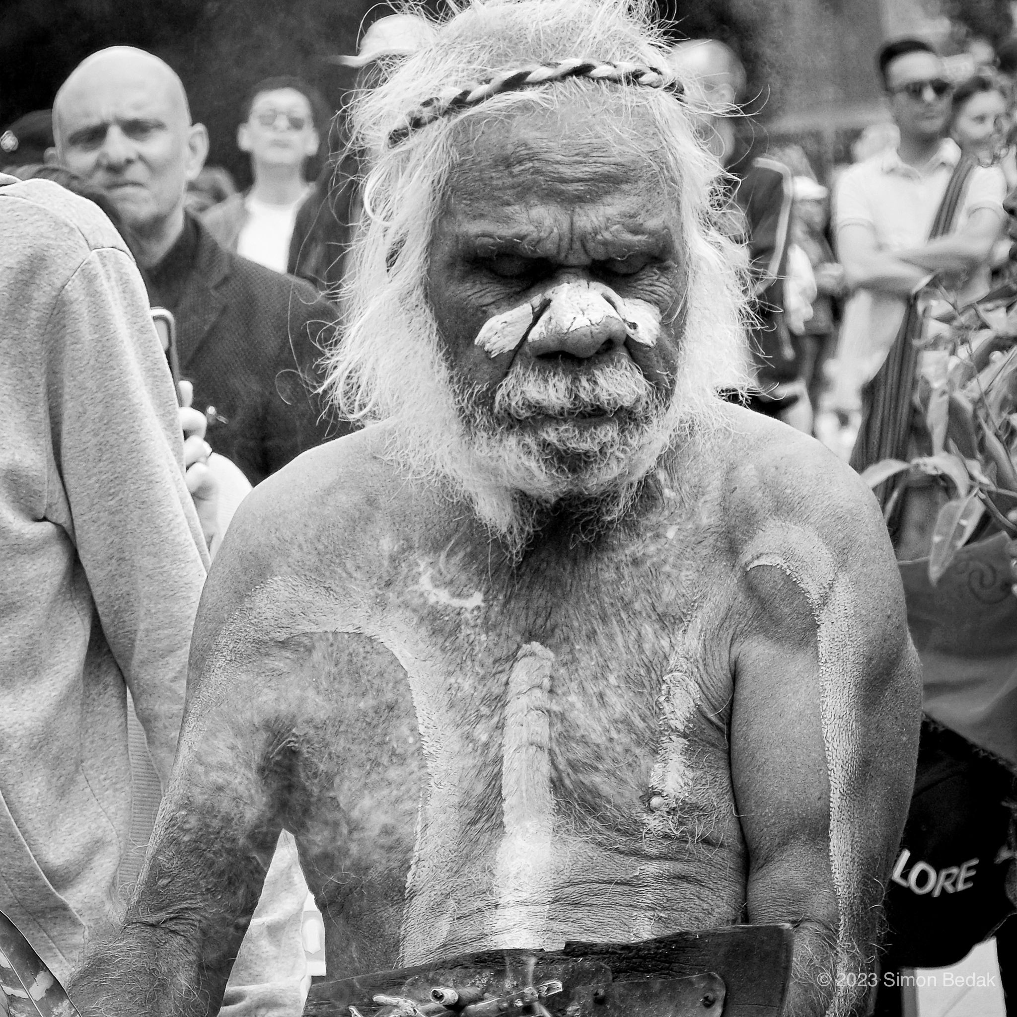 Elderly man with body paint and headband in a crowd.
