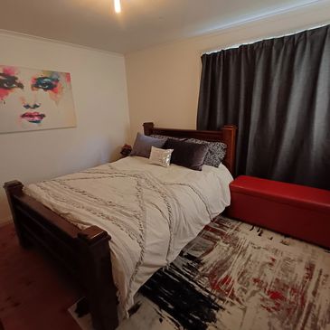 Cozy bedroom with wooden bed, abstract art, and red bench.