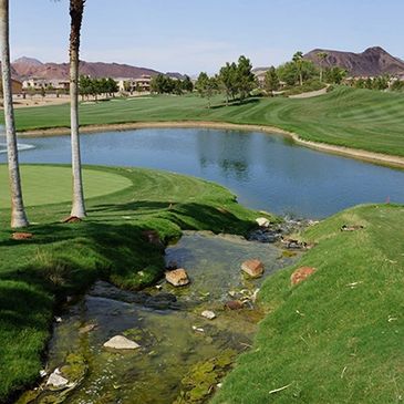 Scenic golf course with water features and desert mountains in the background.