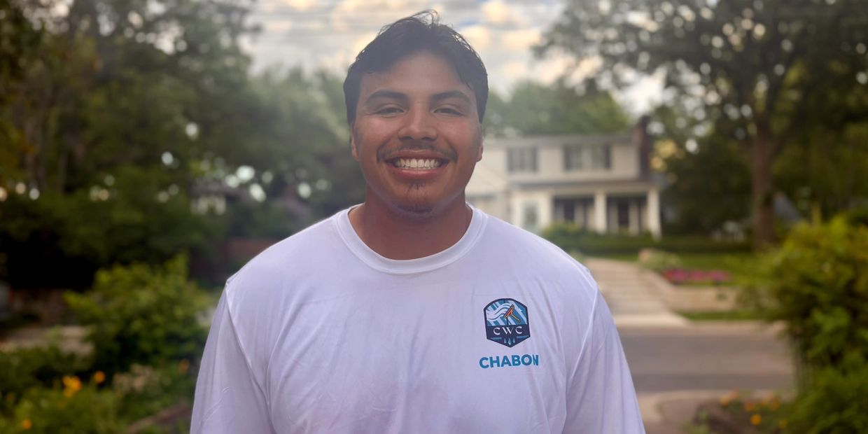 Smiling man outdoors wearing a white shirt with a logo and name 'CHABON'.