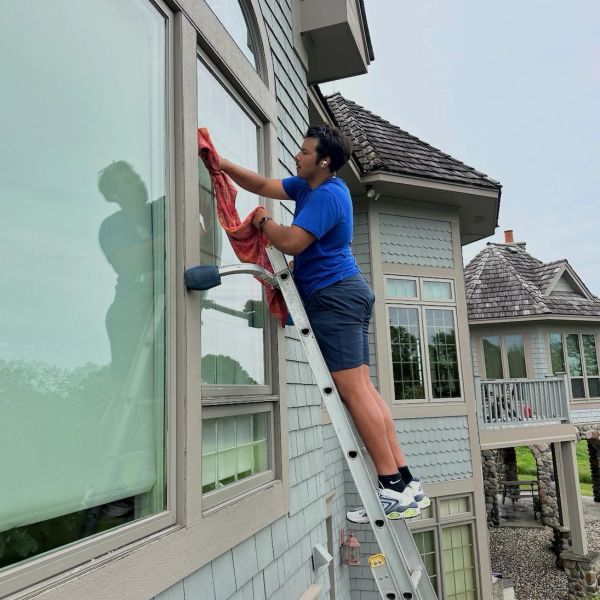 Person cleaning a window while standing on a ladder outside a house.