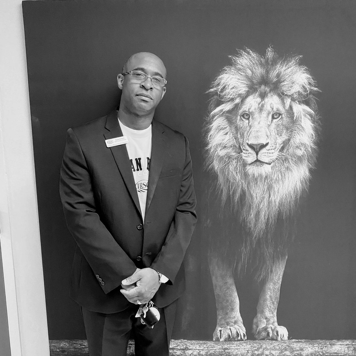Man in suit standing beside a majestic lion portrait.
