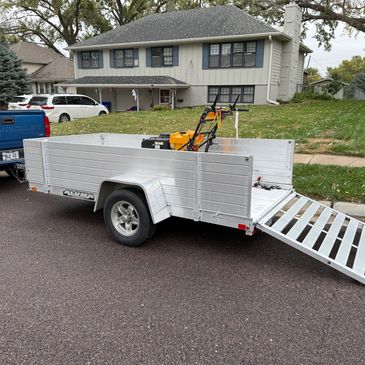 Blue Chevrolet truck towing an aluminum trailer with a lawnmower inside.