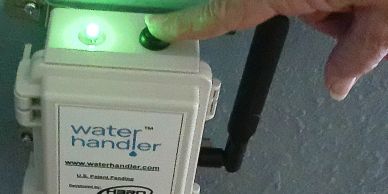 A finger pressing a green-lit button on a device labeled Water Handler.