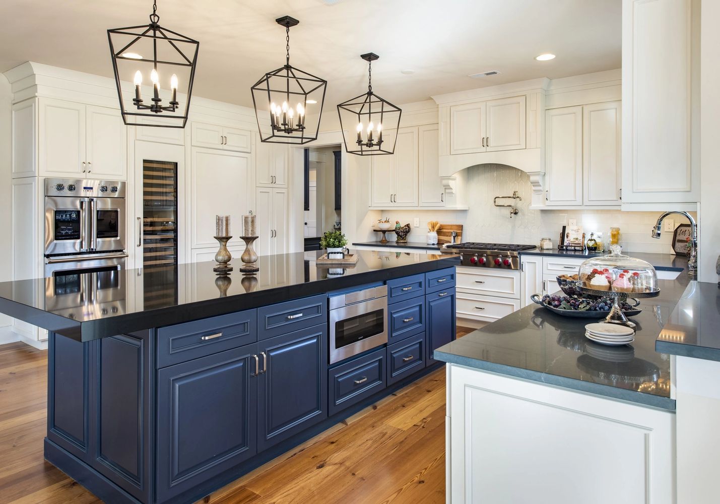 Modern kitchen with navy island and white cabinets under geometric pendant lights.