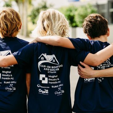 Three kids wearing matching Can-Am Roofing shirts with arms around each other.