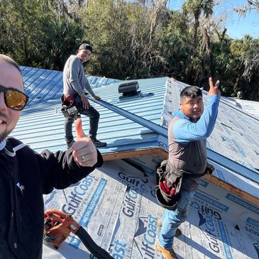 Three men working on a metal roof installation outdoors.