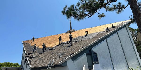 Workers replacing a house roof under clear blue sky.