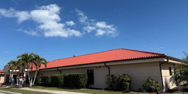 Building with red roof and palm trees under blue sky.