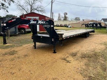 A black Trail Maxx flatbed trailer parked on a gravel driveway.