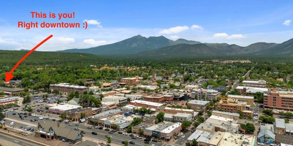 A cityscape with mountains in the background and a red arrow pointing to a location.
