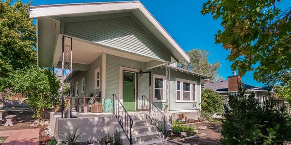 A charming green bungalow with a welcoming porch and lush garden.