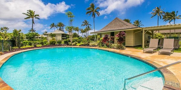 Bright blue swimming pool surrounded by tropical foliage and lounge chairs under a sunny sky.
