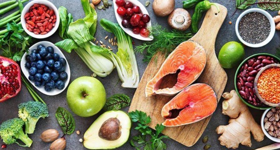 Fresh, colorful healthy foods including salmon, fruits, and vegetables on a table.