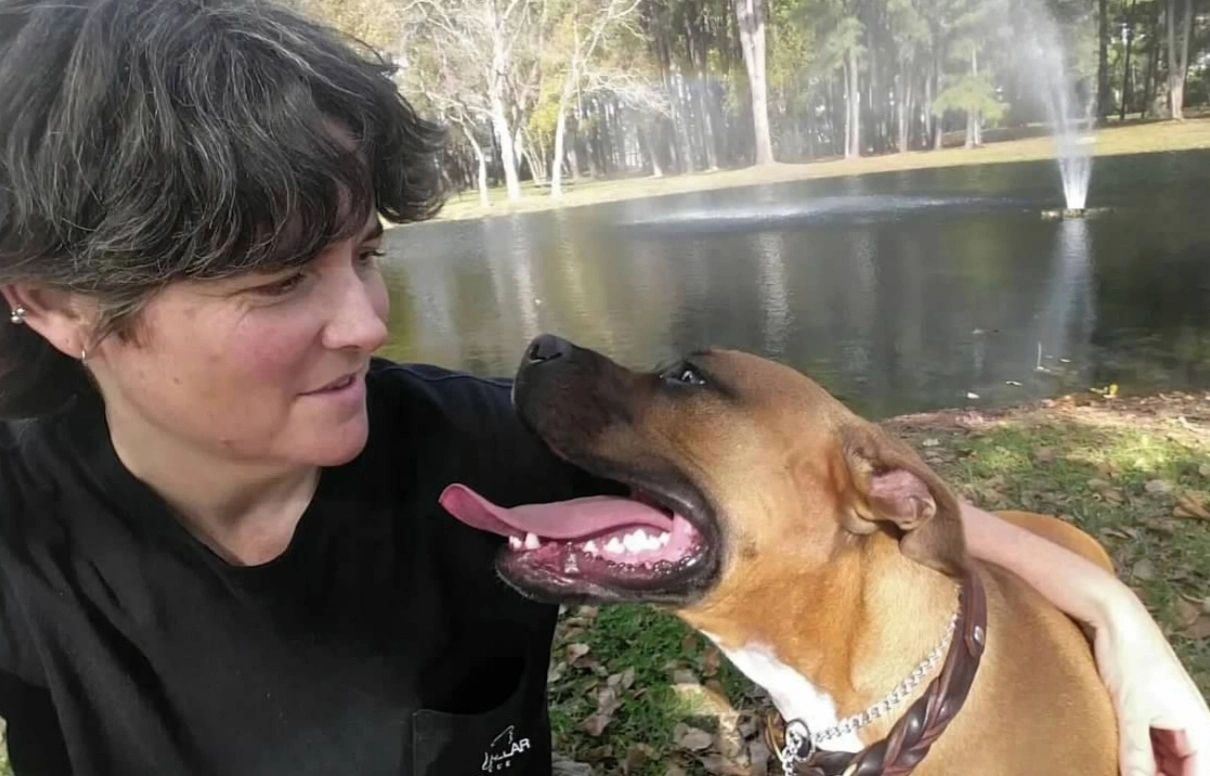 A woman affectionately looks at her happy dog near a pond with fountains.