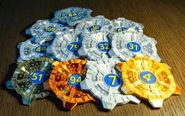 Colorful numbered tokens with mechanical designs on a wooden surface.