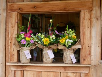 Three flower bouquets in brown paper on a wooden shelf.