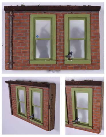 Miniature brick wall with two green-framed windows and bird, showing shadows inside.