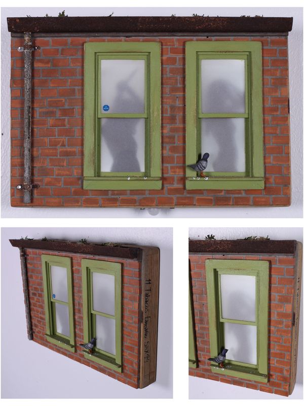 Miniature brick wall with two green-framed windows and bird, showing shadows inside.
