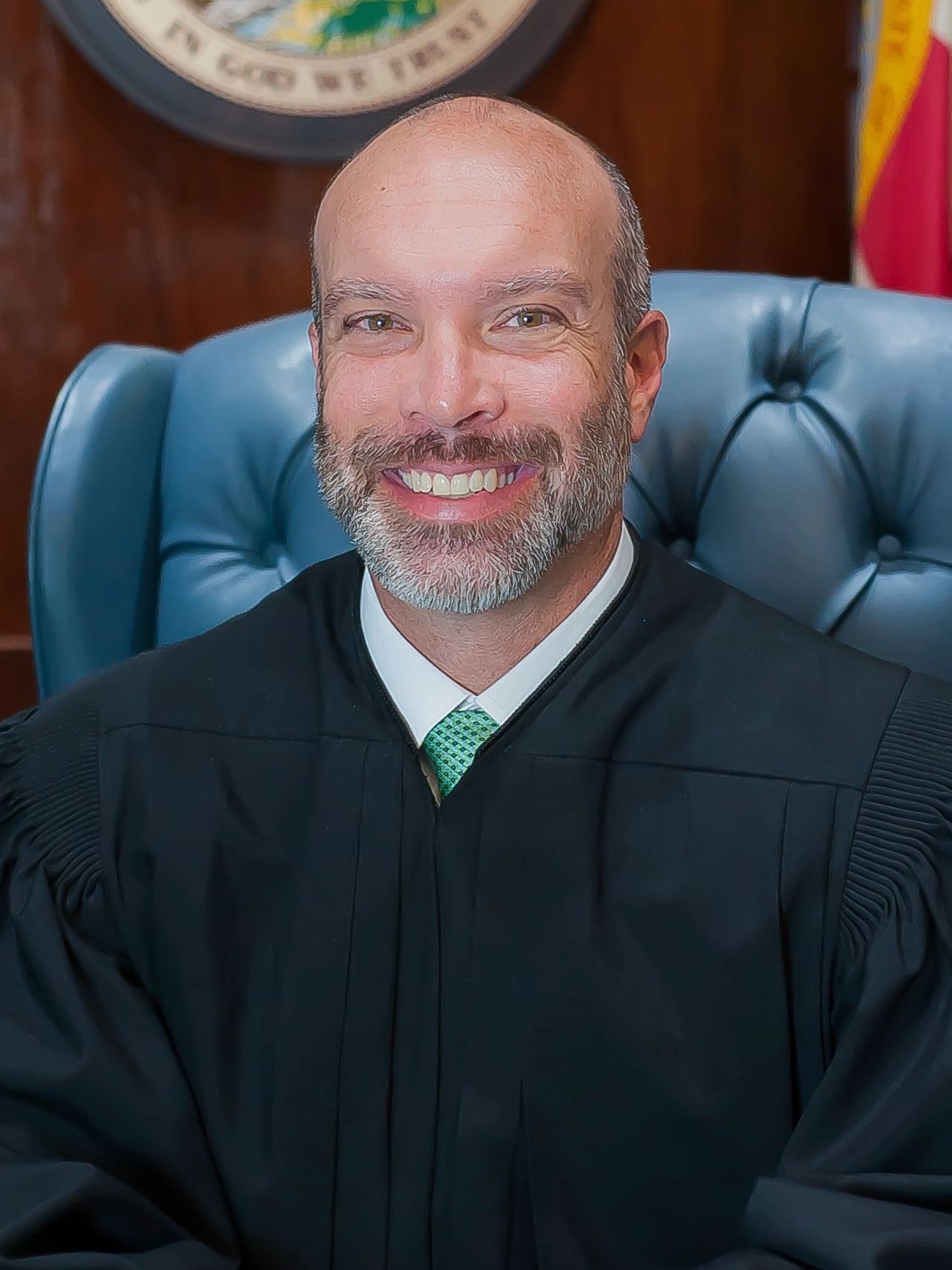 Smiling judge in black robe seated on a blue leather chair.