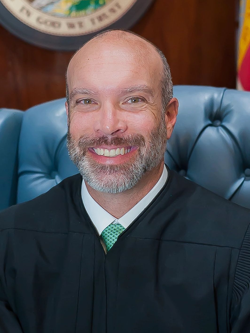 Smiling judge in black robe seated on a blue leather chair.