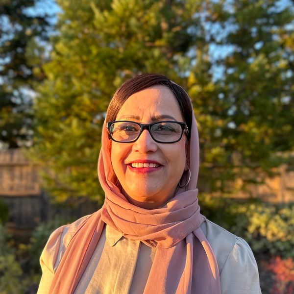 Woman smiling outdoors with glasses and headscarf.