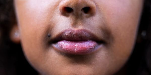 Close-up of a person's lips and lower nose with a beauty mark on the cheek.