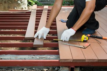 Gloves hands installing brown composite decking planks using a tape measure