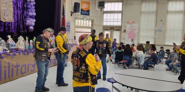 Military veterans interacting with children in a school cafeteria.