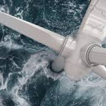 Aerial view of a wind turbine spinning over turbulent ocean water.